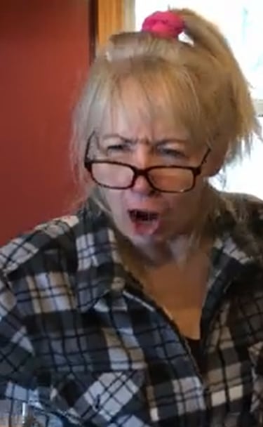 Stella with glasses and a flannel shirt making an angry facial expression in a kitchen.