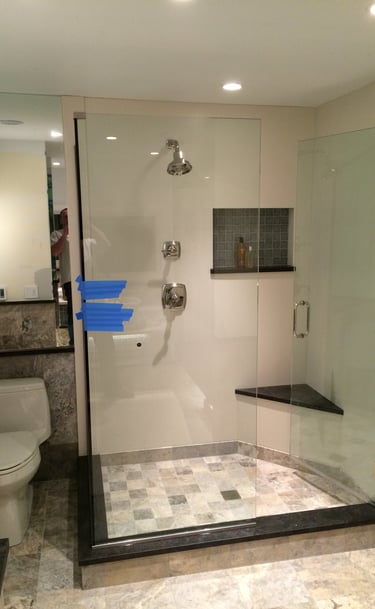 Modern walk-in shower with frameless glass doors, marble tile floor, and a built-in corner bench seat.