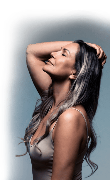 A middle-aged woman with long wavy hair and closed eyes posing for a portrait against a blue background.