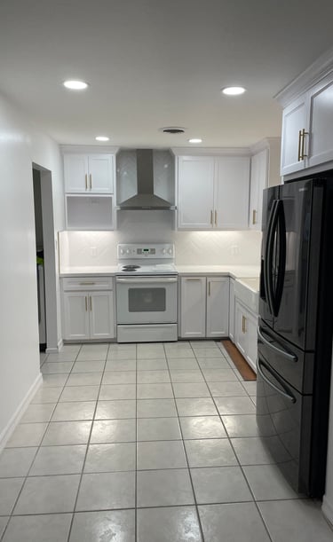 Modern white kitchen with gold hardware, stainless steel range hood, and black refrigerator.