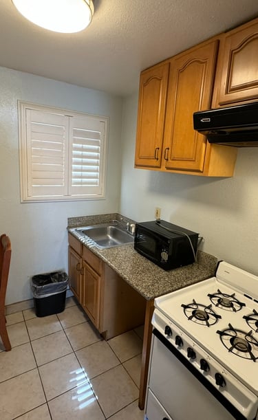 a kitchenette with a stove top, oven, sink, microwave, chair and a table