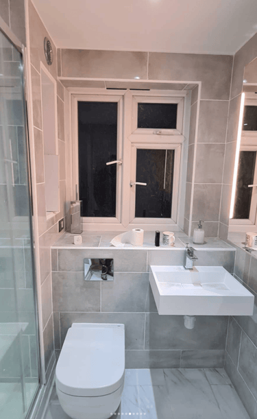 A fully renovated modern bathroom with a sleek glass shower enclosure, wall-mounted toilet, and a mi