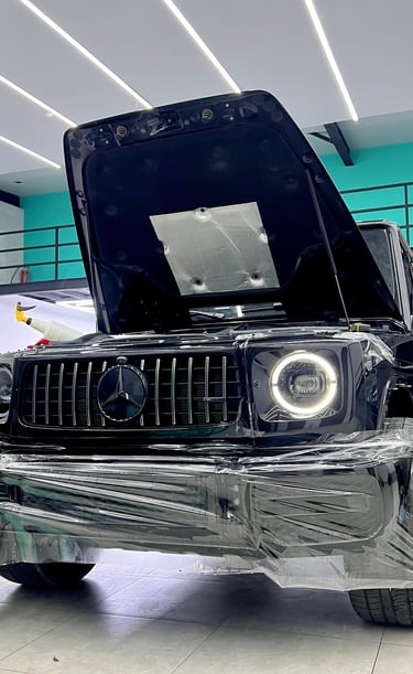 Black Mercedes-Benz G-Wagon receiving a clear paint protection film PPF wrap in a professional detailing shop.
