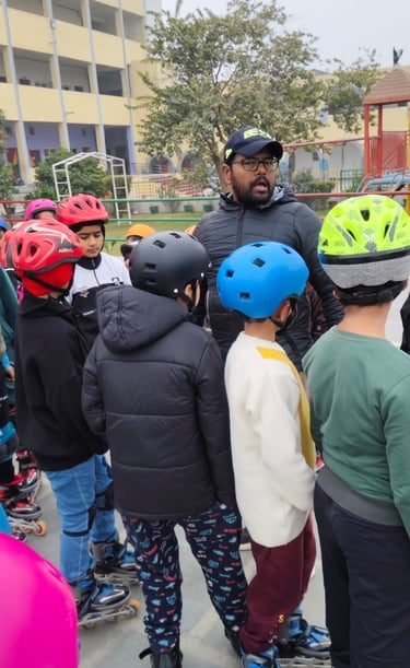 A group of young students in protective helmets and roller skates listen to an instructor at a school skating rink.