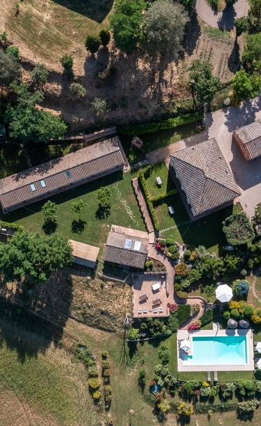 Aerial view of a luxury Italian villa with a blue swimming pool, stone farmhouse, and lush green gardens.