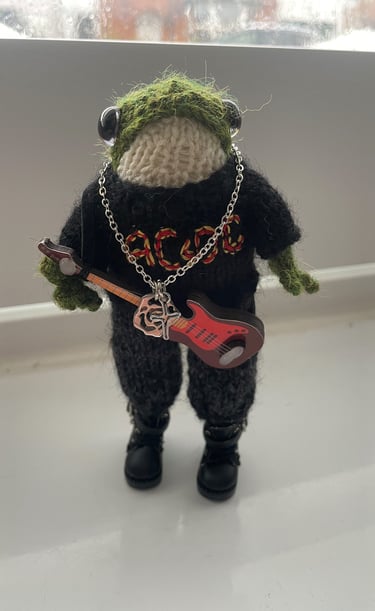 a stuffed frog with a guitar in a knitted jumper with AC/DC on the front 