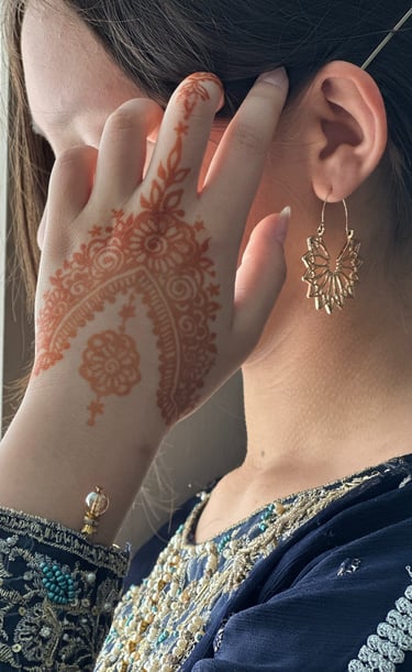 girl with dark hair, wearing a blue beaded tunic, holds hand with henna on it next to her face