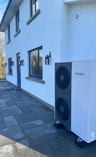 A Vaillant aroTHERM air source heat pump installed on a stone patio outside a white modern home.