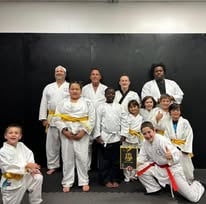 A diverse group of kids and adults posing in white martial arts gis during a karate class.