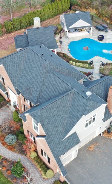 Aerial view of a luxury brick home with a new charcoal asphalt shingle roof and backyard swimming pool.