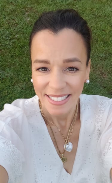 Smiling woman in white lace dress and gold necklaces outdoors against green grass.