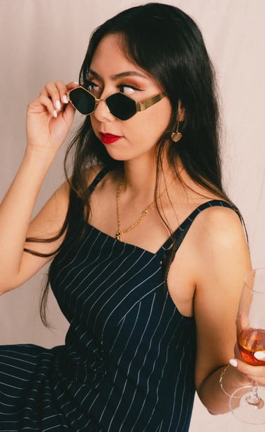 a woman in a dress and sunglasses is holding a drink