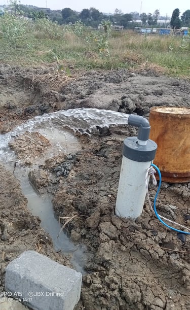 Agricultural water well pump discharging fresh water into a dirt irrigation trench in a field.