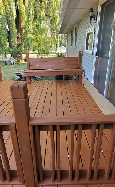 Freshly stained brown wooden deck with built-in benches and railings outside a residential home.