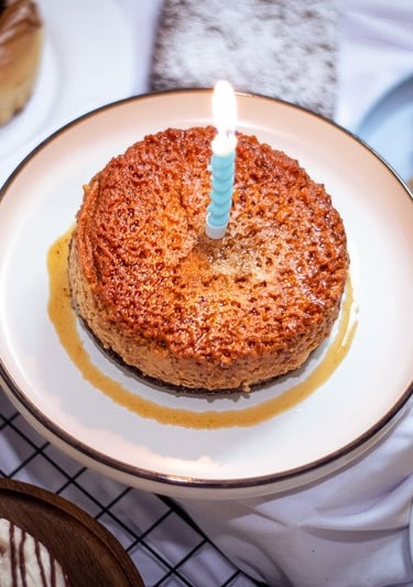 Pastel de flan con caramelo y una vela de cumpleaños encendida, rodeado de una variedad de galletas 
