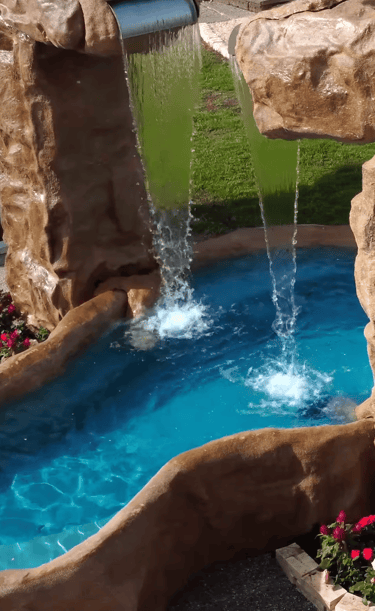 Backyard rock waterfall feature with cascading water flowing into a bright blue swimming pool.