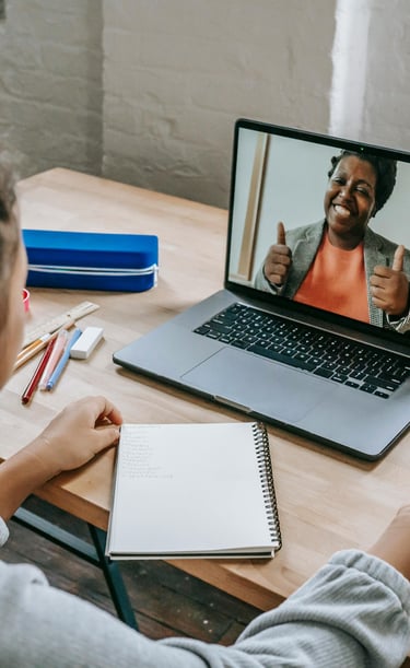 A young student participating in a virtual Tutoring session on a laptop with an encouraging Teacher.