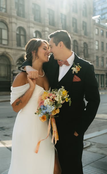 Une mariée et un marié souriants s’enlaçant dans une rue de la ville avec un bouquet coloré de fleur