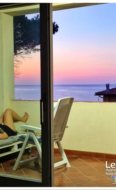 person lying on a chair facing the sea at sunset