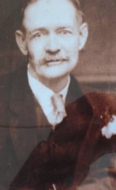 Vintage sepia portrait of an elderly man with a mustache in a formal suit and tie.