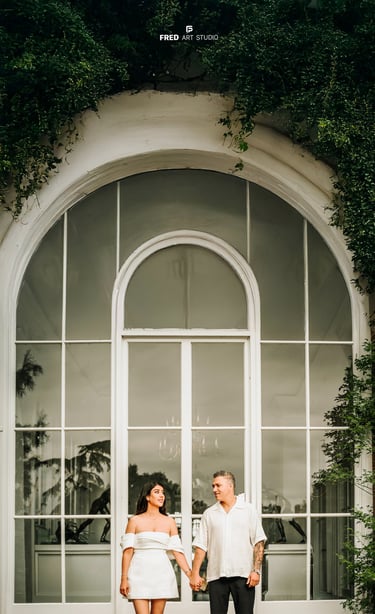 Couple holding hands in front of large white window – engagement photography by Fred Art Studio