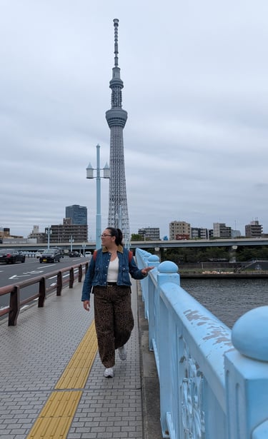 A woman walks on a blue bridge in Tokyo with the Tokyo Skytree tower visible in the background.