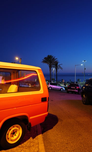 Orange van parked by the seaside at dusk with palm trees in Cascais, Portugal, By ACAT Phot