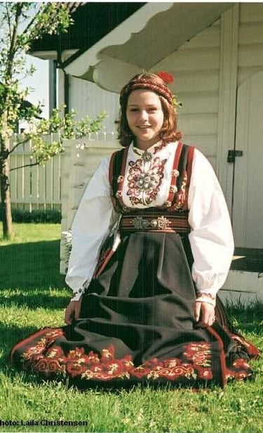 A girl sits in the grass wearing a bunad and head piece