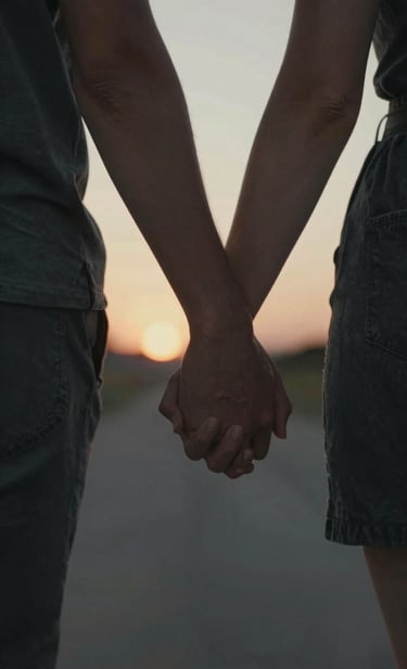 A close-up, cinematic detail shot of two people holding hands during a warm sunset stroll. Focus is on the authentic interaction and natural beauty. The color palette emphasizes rich Charcoal #2C2C2C textures in the background and warm sun-drenched skin tones.