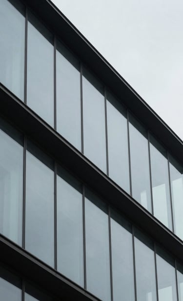 An abstract architectural photograph of a modern building with clean lines and glass textures, reflecting a pale gray sky, sharp focus, minimalist composition, professional and elegant aesthetic.