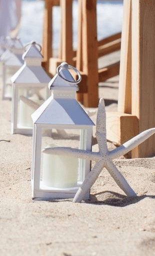 white lantern with candle set on the sand with white starfish
