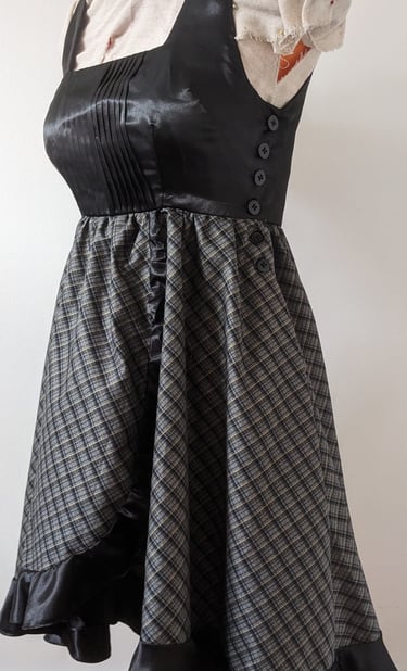 The side of a black/gold plaid and black satin flowy cocktail dress