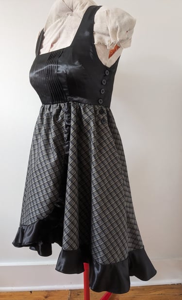 The side of a black/gold plaid and black satin flowy cocktail dress