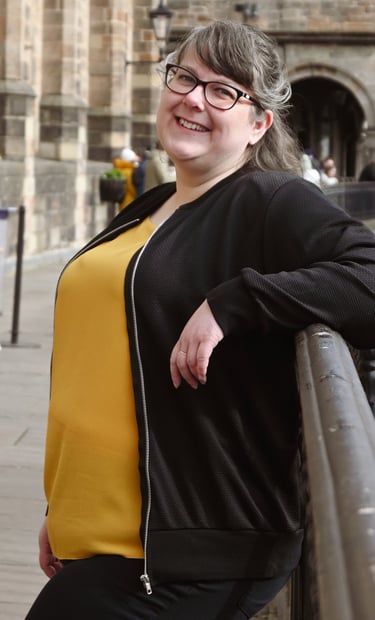 Laura is leaning against a railing with a soft smile on her face, turned towards the camera