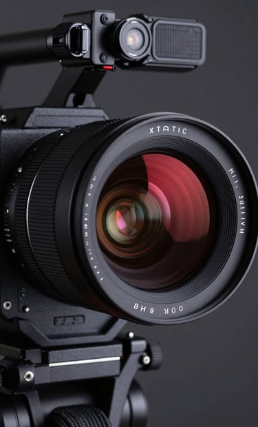 A close-up photograph of a professional cinema camera lens. The glass reflects a sharp deep red neon light against a dark grey studio background. High-end, technical, and moody lighting.