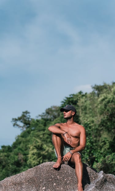 a man sitting on a rock with a hat on