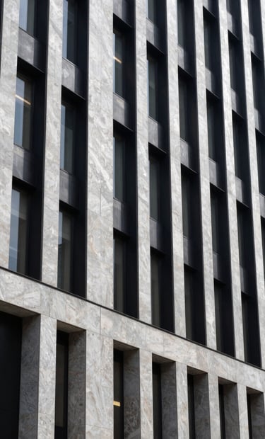A vertical shot showing the exterior facade of a contemporary building in a South American / Brazilian city. The design uses light silver grey stone and deep black steel frames. The lighting is bright and crisp, highlighting the precision of the architectural lines.