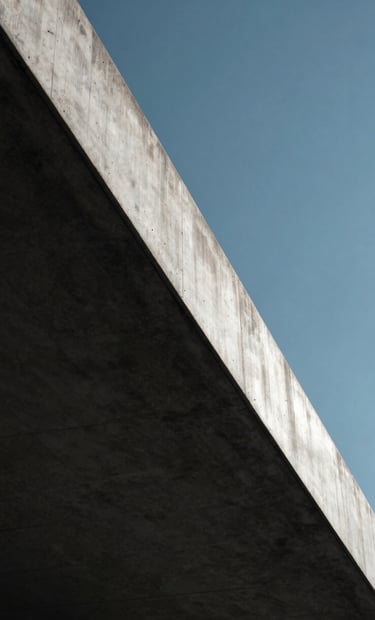 A close-up photograph of a concrete edge meeting a clear sky. The lighting is harsh midday sun creating a sharp division between Midnight Black shadow and Ice White highlights. Sophisticated architectural detail.