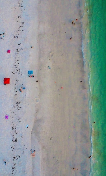 Aerial view of a white sand beach with turquoise ocean water and colorful umbrellas.