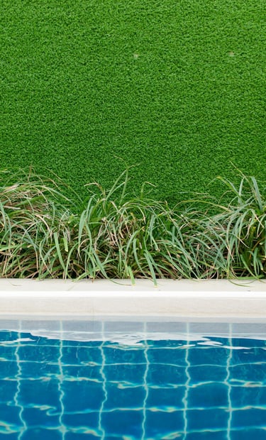 Swimming pool edge with blue water, green plants, and a vibrant artificial grass wall backdrop.