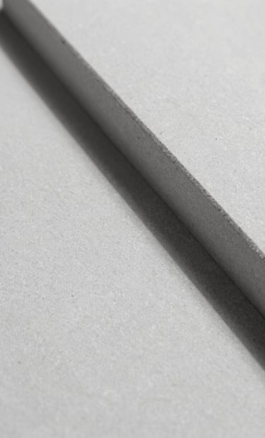 A minimalist macro shot of architectural material, likely smooth light grey stone or textured plaster, with a sharp diagonal shadow cutting across it. High contrast, high-end feel using #F9F7F2 and #333333 tones.