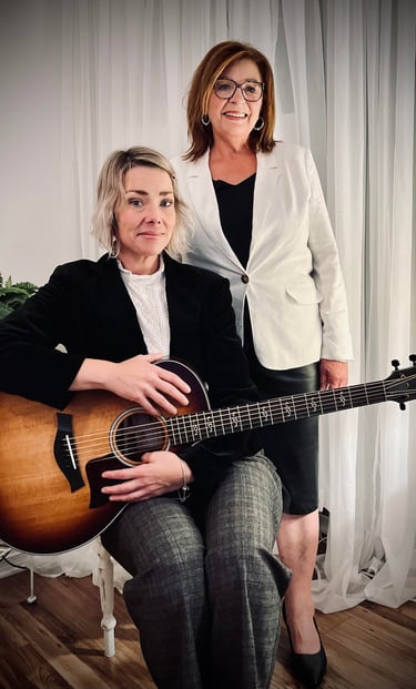 Colette et Caroline Lupien posent, l’une assise avec une guitare, l’autre debout, souriante. 