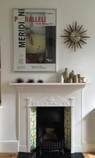 a fireplace with a clock on the mantle, assorted ceramic pieces on display