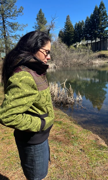 a woman in a green jacket and jeans standing in front of a pond