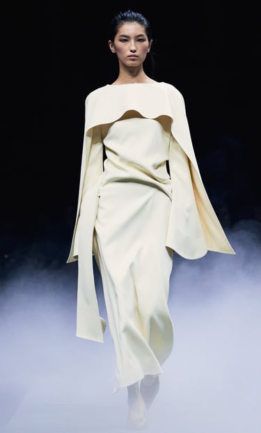 Khaite Spring/Summer 2026 runway model in an ivory long-sleeve gown with cape detail.