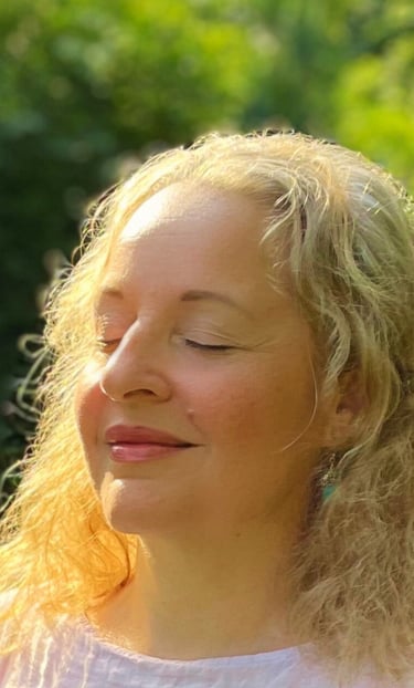 eine lächelnde, blonde Frau mit geschlossenen Augen im Grünen