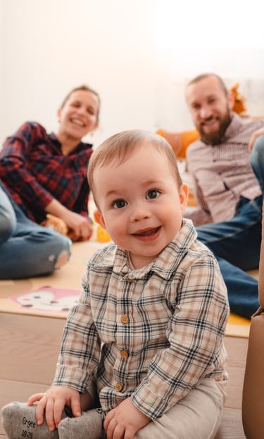 mala beba, iza nje sjede nasmiješeni roditelji