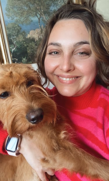 a woman in a hot pink sweater holding a golden doodle puppy with art in the background in portland