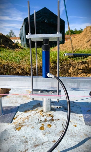 A blue hydraulic jack testing the load capacity of a metal ground screw foundation at a construction site.
