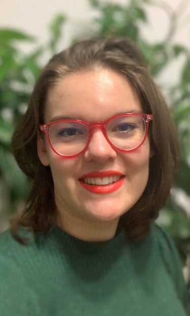 A portrait of a woman with shoulder-length brown hair, wearing red glasses and a green top, smiling